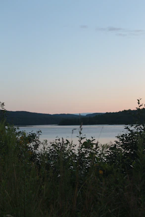 A serene view of Loch Lomond at sunset with Cameron House nestled among lush greenery.