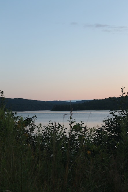 Sunset view over a serene lake with a cozy lakeside retreat surrounded by gentle hills.