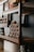 Wooden shelves display rows of small jars and various bottles. The jars are stacked in a pyramid shape, each labeled, suggesting they contain products like creams or condiments. The rustic wooden design paired with the neatly arranged items creates an organized and artisanal appearance.