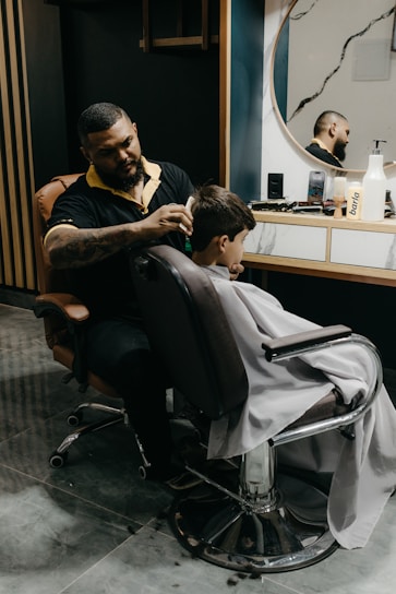 A skilled barber carefully shaping a young boy's haircut in a bright, friendly barbershop setting.