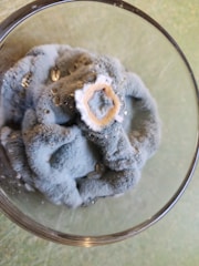 A fuzzy, blue-gray mold has formed in a circular pattern on the surface of a liquid in a clear glass container. The mold has a central off-white spot, and there are some small droplets of liquid visible on its surface.