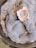 A close-up of mold growth with a circular pattern in shades of grey and blue, featuring a central area with a distinct peach and white outline. Small droplets of moisture are scattered across the fuzzy surface, giving it a textured appearance.