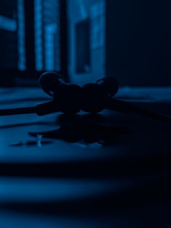 A set of earphones is placed on a surface, with a close-up view highlighting their silhouette. The background is slightly blurred, showcasing an abstract pattern created by light and shadow coming through a window.