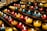 Rows of small, colorful candle holders containing lit candles are arranged neatly on metal shelves. The candles emit a warm, glowing light, creating a serene and peaceful atmosphere.