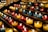 Rows of small, colorful candle holders containing lit candles are arranged neatly on metal shelves. The candles emit a warm, glowing light, creating a serene and peaceful atmosphere.