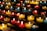 Rows of small, colorful candles are lit and arranged on black metal shelves. The candles are contained in glass holders of various colors, including red, yellow, and blue. The soft glow from the flames creates a warm and serene atmosphere.