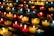 Rows of small, colorful candles are lit and arranged on black metal shelves. The candles are contained in glass holders of various colors, including red, yellow, and blue. The soft glow from the flames creates a warm and serene atmosphere.
