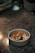 A dessert is beautifully arranged in a white bowl, placed on a granite surface. The dish includes a cream-like substance topped with an intricate caramel decoration and crumbled bits.