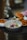 A bowl of ceviche garnished with red onion, edible flowers, and herbs is accompanied by a plate of sweet potato fries and a sandwich. The dish is artfully presented on a dark tray with a blurred background, creating an elegant dining atmosphere.