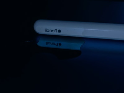 A close-up of a white stylus with the brand logo and 'pencil' printed on the side. It is lying on a reflective surface, creating a clear mirror image.