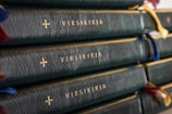 A stack of dark green leather-bound books with gold lettering and crosses embossed on the spine. Each book has several colorful ribbon bookmarks hanging from the top.