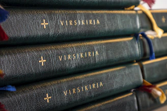 A stack of well-loved hardcover Christian books with a Coptic cross pendant resting on top.