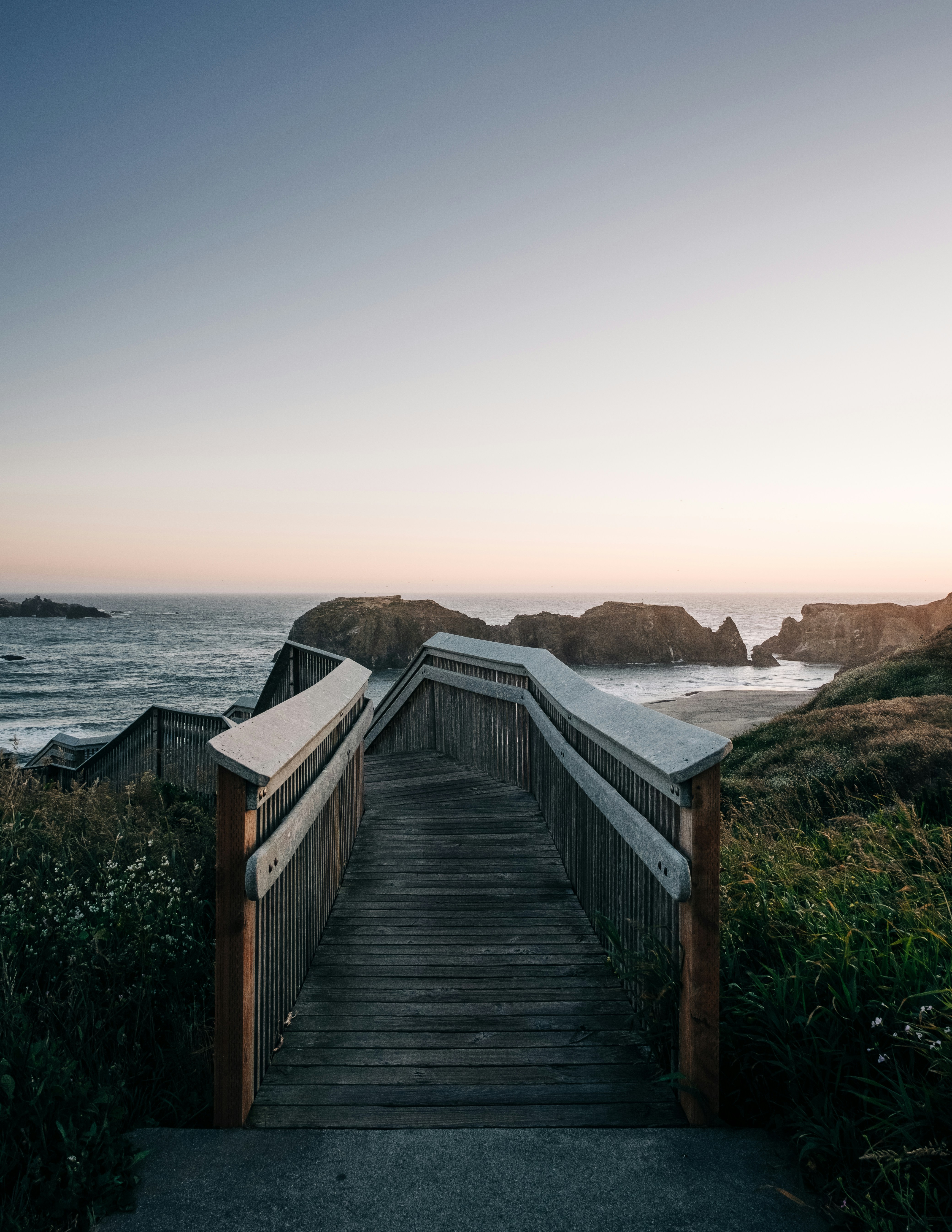 a wooden walkway leading to the ocean at sunset