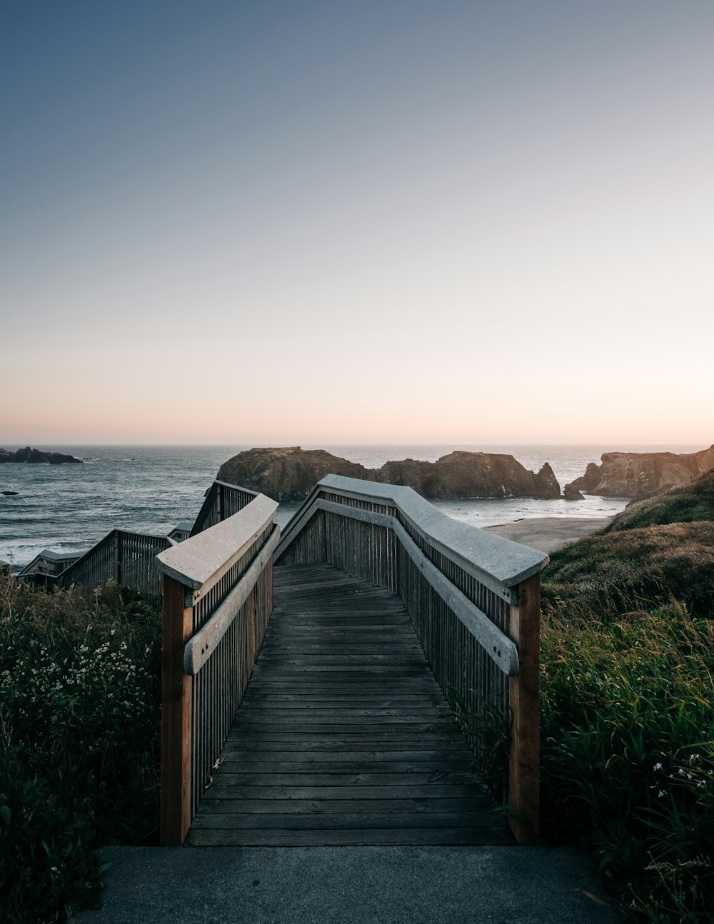 a wooden walkway leading to the ocean at sunset