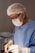 A surgeon is focused on an operation, wearing protective gear including a mask, gloves, and a hair cap. The hands are stained with blood, indicating active involvement in a surgical procedure. Medical instruments are visible, highlighting the clinical setting.