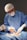 A medical professional wearing a blue surgical gown, mask, and hair net is performing surgery. The hands are gloved, and the surroundings are sterile, indicating an operating room setting. Instruments are being used, and there is a focus on a particular area of a patient's body, covered with surgical drapes.