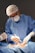 A medical professional wearing a blue surgical gown, mask, and hair net is performing surgery. The hands are gloved, and the surroundings are sterile, indicating an operating room setting. Instruments are being used, and there is a focus on a particular area of a patient's body, covered with surgical drapes.