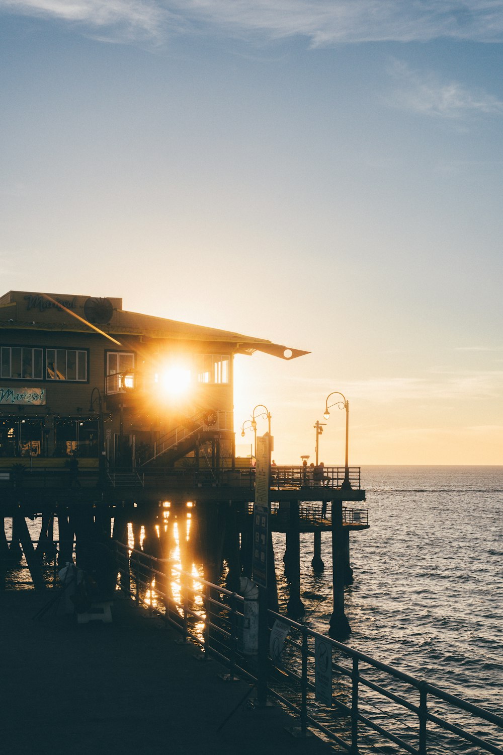 the sun is setting on a pier by the ocean