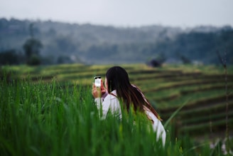 A farmer checking a smartphone displaying weather alerts in a lush green field.