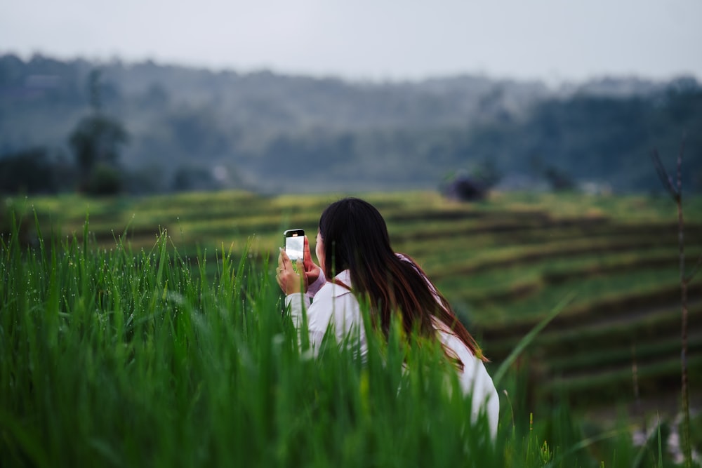 a woman taking a picture of a field with a cell phone