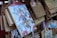 An illustration featuring animated characters with various expressions, surrounded by colorful attire and floral headpieces, is prominently displayed on a wooden plaque. This plaque is among several hanging wooden tablets, each featuring Japanese writing and some vivid illustrations.