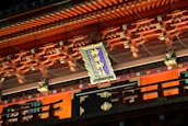 An ornate building facade richly decorated with colorful wooden elements and intricate designs. A prominently displayed sign with Japanese characters is centered, surrounded by traditional architectural details and lion-like figures.