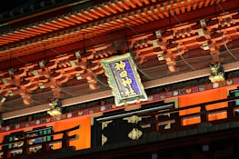 An ornate building facade richly decorated with colorful wooden elements and intricate designs. A prominently displayed sign with Japanese characters is centered, surrounded by traditional architectural details and lion-like figures.
