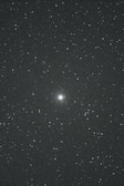A night sky filled with countless stars. In the center, there is a brighter celestial object, possibly a galaxy or nebula, standing out against the dark backdrop. The vast, deep space evokes a sense of wonder and mystery.