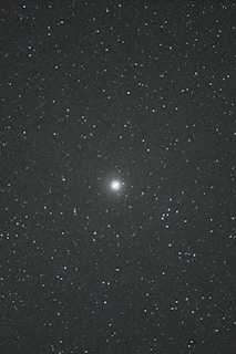 A night sky filled with countless stars. In the center, there is a brighter celestial object, possibly a galaxy or nebula, standing out against the dark backdrop. The vast, deep space evokes a sense of wonder and mystery.