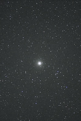 A night sky filled with countless stars. In the center, there is a brighter celestial object, possibly a galaxy or nebula, standing out against the dark backdrop. The vast, deep space evokes a sense of wonder and mystery.