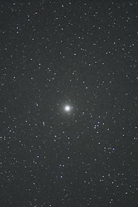 A night sky filled with countless stars. In the center, there is a brighter celestial object, possibly a galaxy or nebula, standing out against the dark backdrop. The vast, deep space evokes a sense of wonder and mystery.