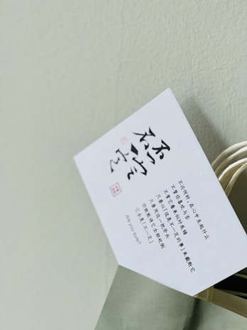 A white card with printed text in Chinese characters and some English text, partially inserted into a light green paper bag with a twisted handle. The background is a plain light-colored wall.