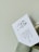 A white card with printed text in Chinese characters and some English text, partially inserted into a light green paper bag with a twisted handle. The background is a plain light-colored wall.