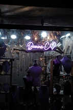 A shop window display featuring several mannequins adorned with jewelry. The backdrop is filled with hanging necklaces and various decorative elements. A neon sign with the words 'Donna C' and a heart symbol is prominently visible in the center.