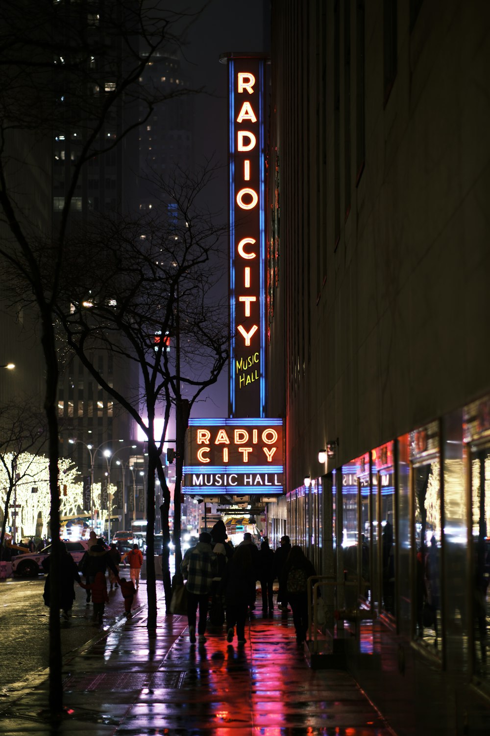 a city street at night with people walking on the sidewalk