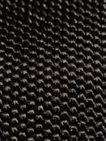A close-up of a textured woven material displaying a pattern of small interlocking fibers with a glossy sheen under light.