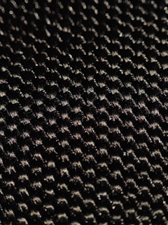 A close-up of a textured woven material displaying a pattern of small interlocking fibers with a glossy sheen under light.