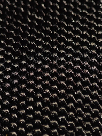 A close-up of a textured woven material displaying a pattern of small interlocking fibers with a glossy sheen under light.