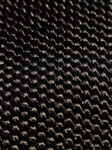 A close-up of a textured woven material displaying a pattern of small interlocking fibers with a glossy sheen under light.