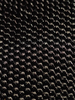 A close-up of a textured woven material displaying a pattern of small interlocking fibers with a glossy sheen under light.