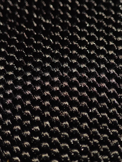 A close-up of a textured woven material displaying a pattern of small interlocking fibers with a glossy sheen under light.