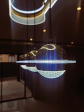 Three spherical pendant lights hang from the ceiling in a row, each featuring a crystal-like lower half and a smooth, reflective upper half. The lighting fixtures emit a bright, cool illumination, casting reflections on the nearby surfaces. The background is dimly lit, enhancing the aesthetic appeal of the lights.