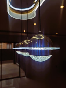 Three spherical pendant lights hang from the ceiling in a row, each featuring a crystal-like lower half and a smooth, reflective upper half. The lighting fixtures emit a bright, cool illumination, casting reflections on the nearby surfaces. The background is dimly lit, enhancing the aesthetic appeal of the lights.