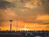 Wide shot of crowds gathered in the square under a dramatic sunset sky.