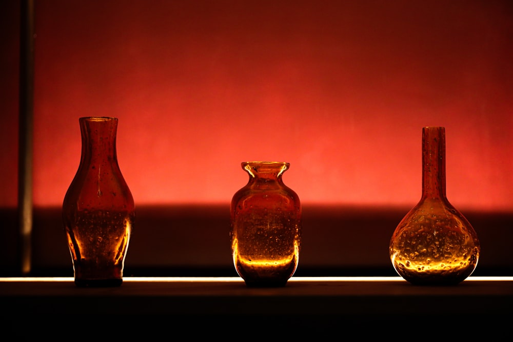 three glass vases sitting on a table in front of a red wall