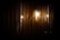 A spherical wall-mounted light fixture emits a warm glow, reflecting against a series of vertical, textured metallic or wooden panels. The lighting creates a subtle play of shadows and highlights, giving a cozy and intimate ambiance.