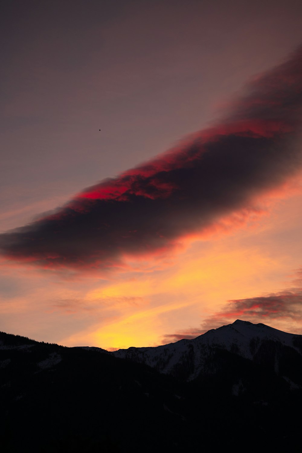 a red cloud is in the sky over a mountain