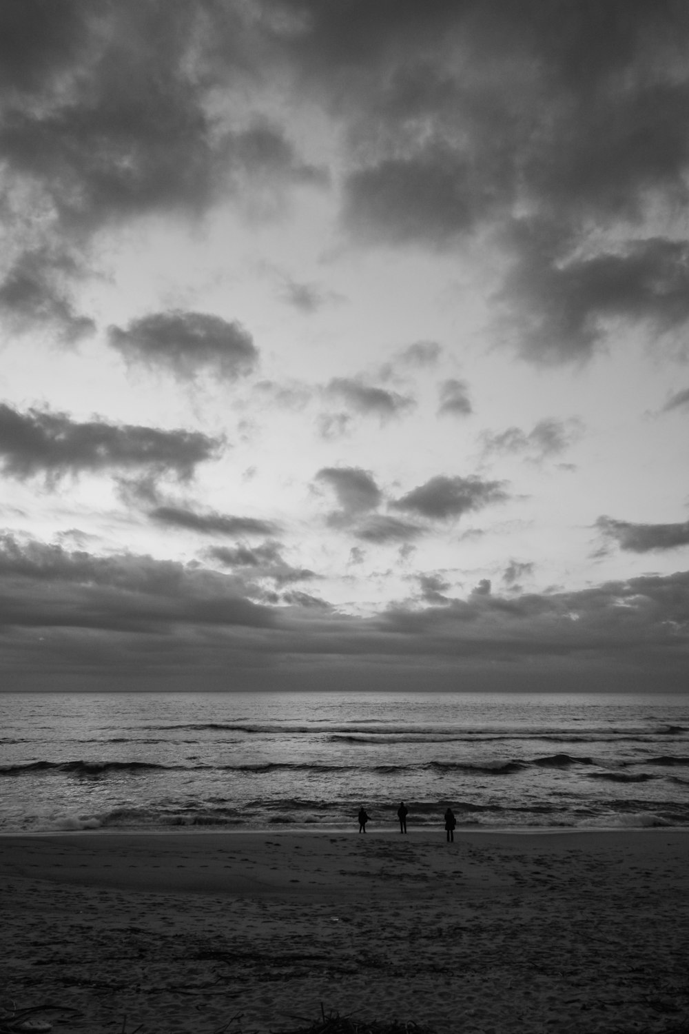 a couple of people standing on top of a beach under a cloudy sky