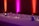 A long table is decorated with delicate string lights and small decorative objects. The background features colorful lighting with a gradient of pink, purple, and orange hues on the walls, creating a cozy and inviting atmosphere.
