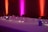A long table is decorated with delicate string lights and small decorative objects. The background features colorful lighting with a gradient of pink, purple, and orange hues on the walls, creating a cozy and inviting atmosphere.